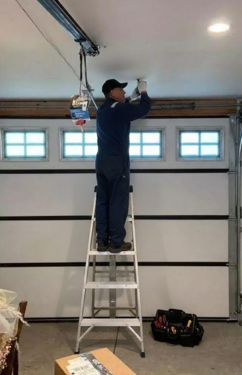 Technician on a ladder repairing a garage door opener track