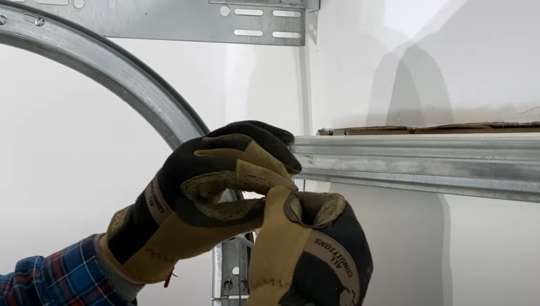 Close-up of a technician's gloved hands adjusting garage door spring hardware
